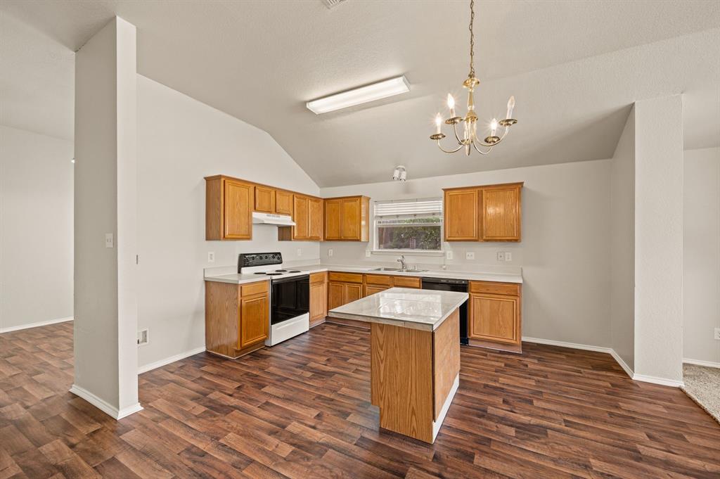 5509 Timber Ridge Court Watauga, TX 76137 - Photo 13 of 28 Kitchen featuring wood-finish flooring, a central island with a light-toned countertop, wood cabinetry, built-in appliances, and a vaulted ceiling