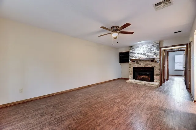 a view of a room a fireplace a ceiling fan and wooden floor