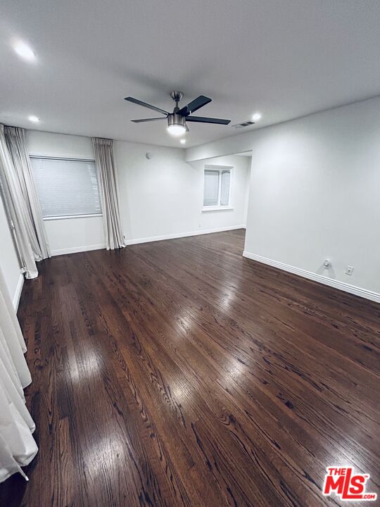 a view of an empty room with wooden floor and a ceiling fan