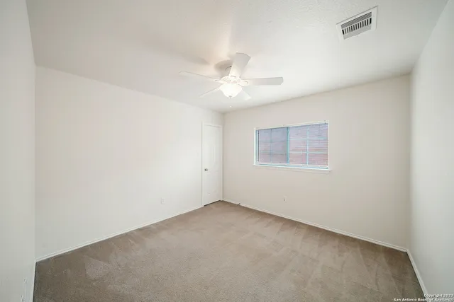 an empty room with a chandelier fan and windows