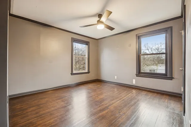 an empty room with wooden floor chandelier fan and windows