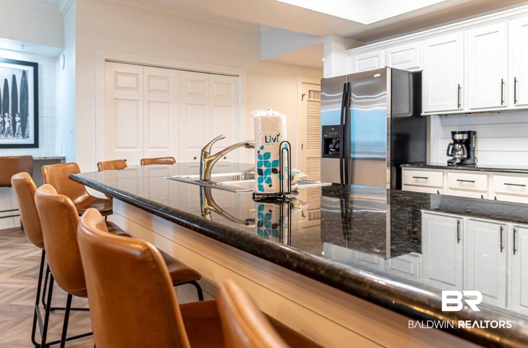 27800 Canal Road, Unit 212 Orange Beach, AL 36561 - Photo 7 of 43 Kitchen with crown molding, dark stone countertops, white cabinetry, stainless steel refrigerator with ice dispenser, and a kitchen breakfast bar