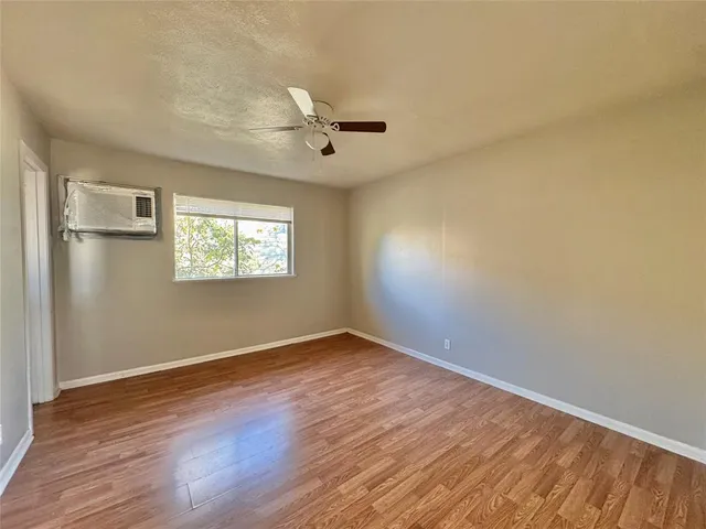 an empty room with wooden floor chandelier fan and windows