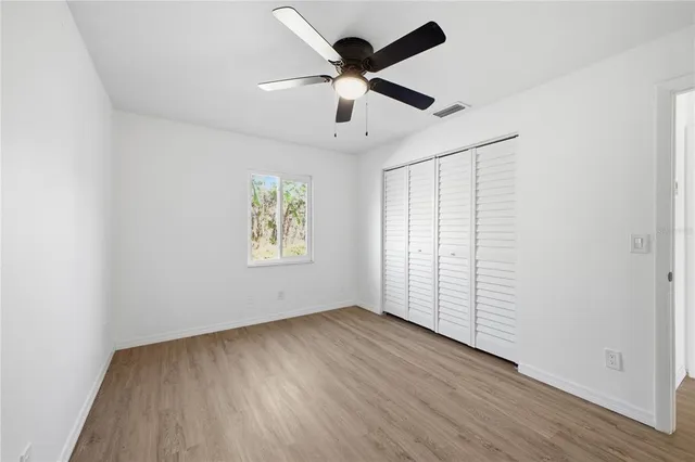 an empty room with wooden floor chandelier fan and windows
