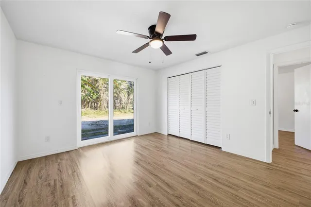 an empty room with wooden floor chandelier fan and windows