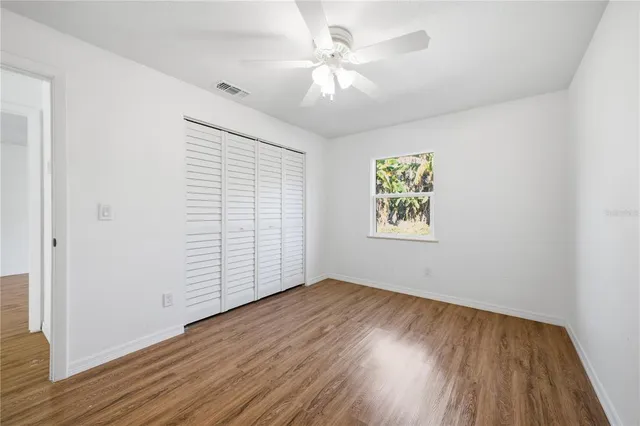 an empty room with wooden floor chandelier fan and windows