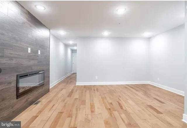 a view of an empty room with wooden floor and a kitchen