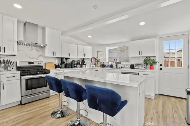 a kitchen with stainless steel appliances kitchen island granite countertop a stove a sink a refrigerator and white cabinets with wooden floor