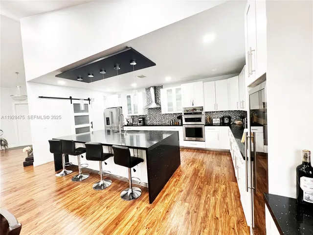 a kitchen with stainless steel appliances granite countertop a refrigerator a sink dishwasher a stove and white countertops with wooden floor