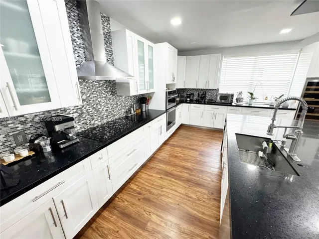 a large white kitchen with granite countertop a stove a sink and white cabinets with wooden floor