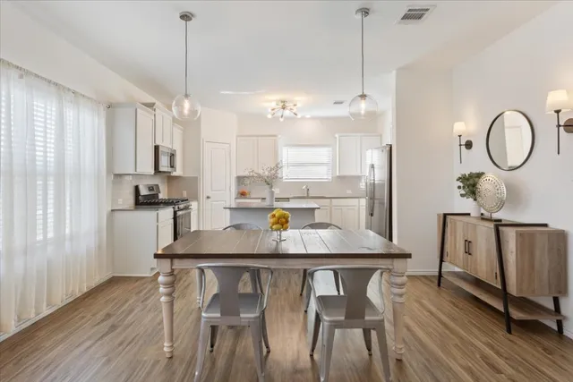 a kitchen with stainless steel appliances granite countertop a stove a refrigerator a sink a dining table and chairs with wooden floor