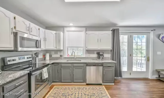 a kitchen with stainless steel appliances granite countertop a stove a sink dishwasher a microwave oven and a dining table with wooden floor