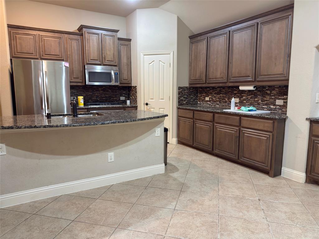 1017 Knoxbridge Road Forney, TX 75126 - Photo 10 of 16 a large kitchen with granite countertop a stove top oven a sink dishwasher and a refrigerator with wooden cabinets