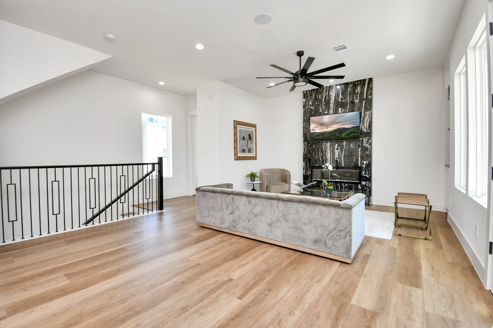 2512 Gray Street Houston, TX 77003 - Photo 11 of 46 This modern living area features hardwood floors, a striking black marble accent wall with a mounted TV, and a sleek ceiling fan. The space is bright with large windows and includes a stylish gray couch and accent chair, creating a cozy yet sophisticated atmosphere.