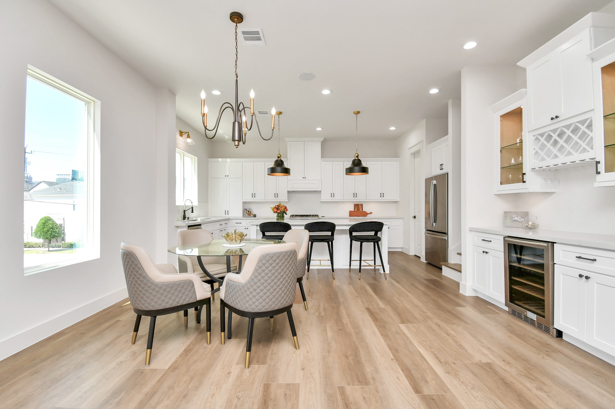2512 Gray Street Houston, TX 77003 - Photo 15 of 46 This bright, modern kitchen features white cabinetry, a large island with seating, and elegant light fixtures. The open layout includes a cozy dining area with upholstered chairs, wood flooring, and ample natural light from a large window.