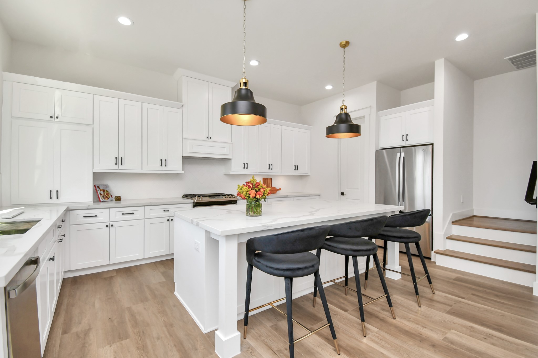 2512 Gray Street Houston, TX 77003 - Photo 18 of 46 This kitchen features a modern design with white cabinetry and sleek countertops. It includes stainless steel appliances, an island with seating for three, stylish pendant lighting, and hardwood flooring, creating a bright and inviting space.
