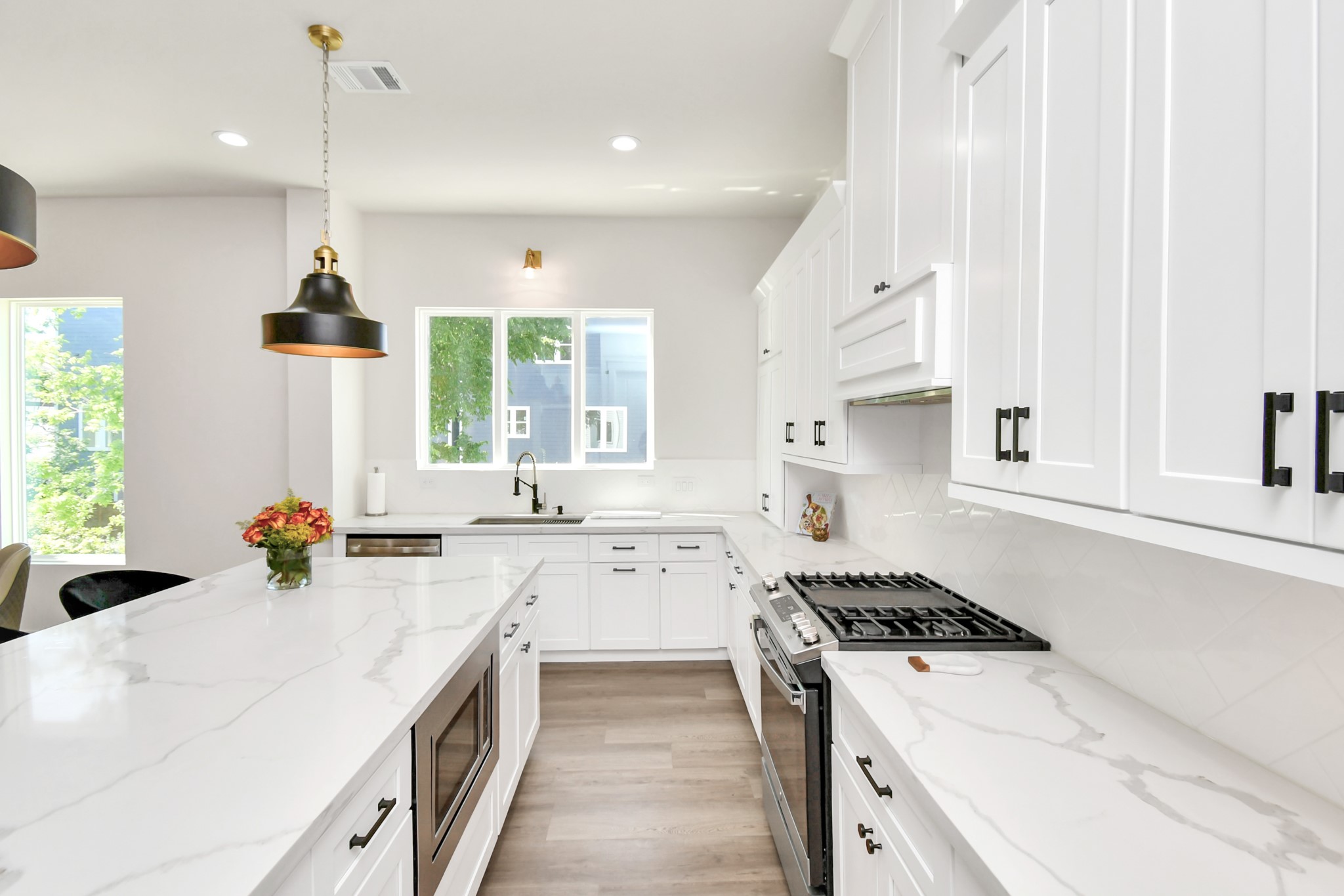 2512 Gray Street Houston, TX 77003 - Photo 21 of 46 This modern kitchen features sleek white cabinetry, marble countertops, and stainless steel appliances. It has a spacious island with a built-in microwave and stylish pendant lighting, creating a bright and inviting space perfect for cooking and entertaining.