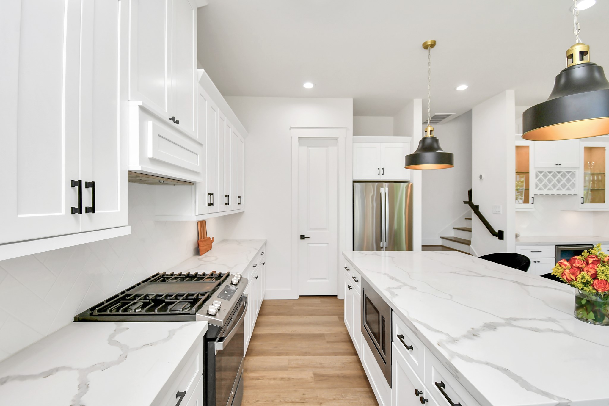 2512 Gray Street Houston, TX 77003 - Photo 23 of 46 This modern kitchen features sleek white cabinetry, a spacious marble countertop island, stainless steel appliances, and stylish pendant lighting, creating a bright and inviting space perfect for cooking and entertaining.