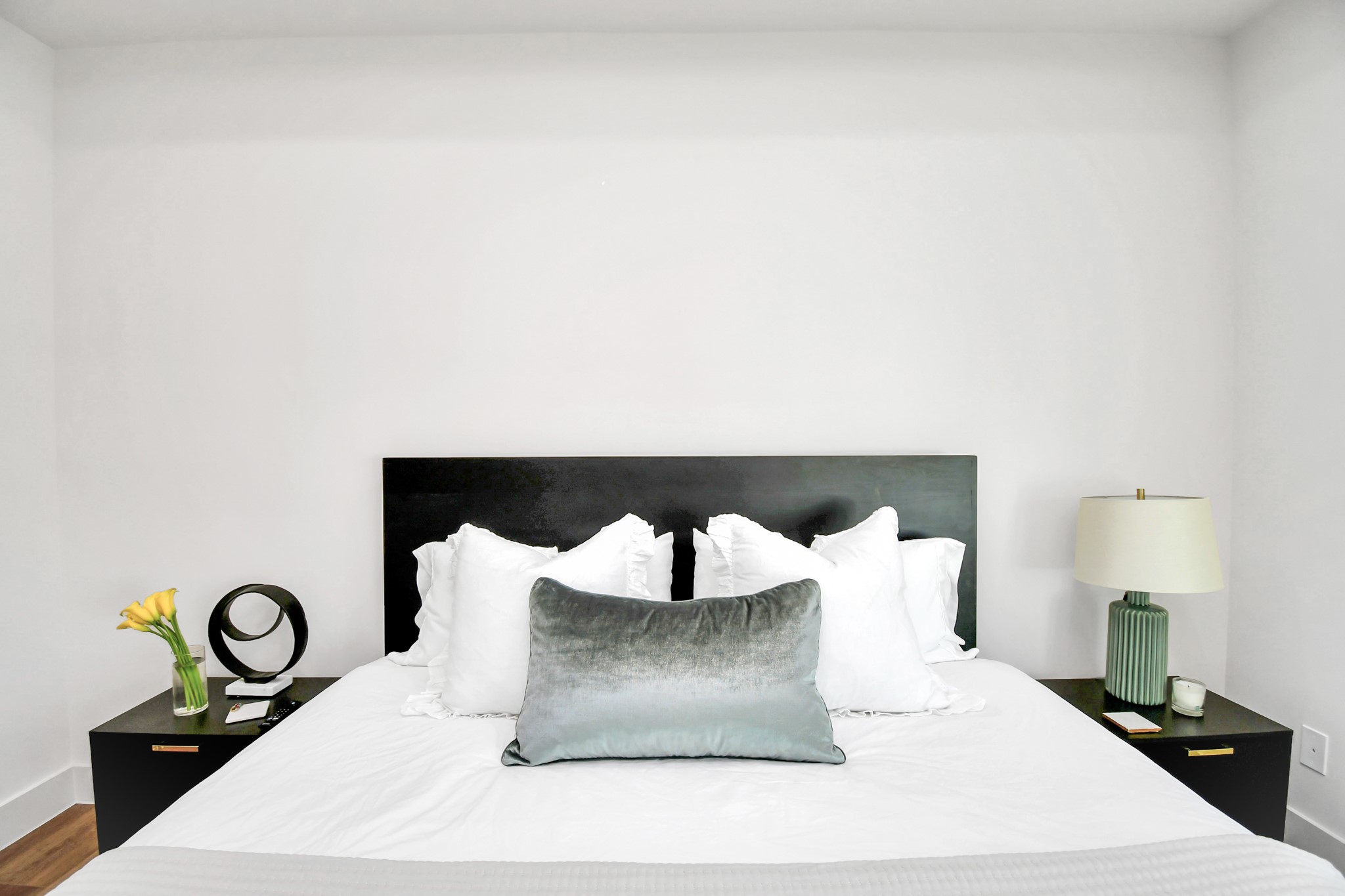 2512 Gray Street Houston, TX 77003 - Photo 27 of 46 This bedroom features a minimalist design with a modern black headboard, white bedding, and a plush gray accent pillow. Two sleek nightstands flank the bed, each with stylish decor, including a lamp and fresh flowers, creating a serene and inviting space.