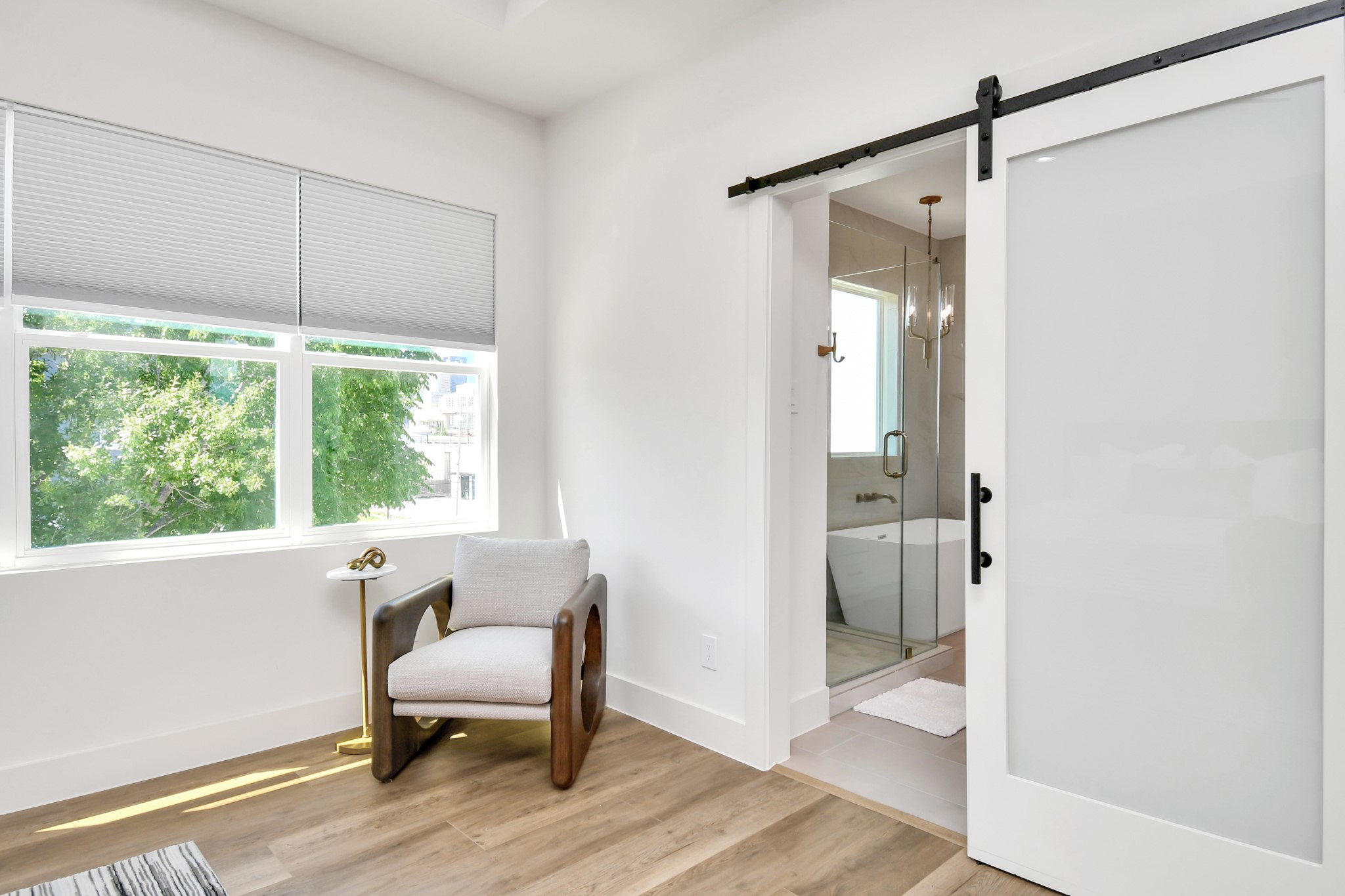 2512 Gray Street Houston, TX 77003 - Photo 29 of 46 Bright room with large windows and a view of greenery, featuring light wood flooring. Includes a modern armchair and a sleek glass sliding door leading to a bathroom with a tub and glass shower enclosure.