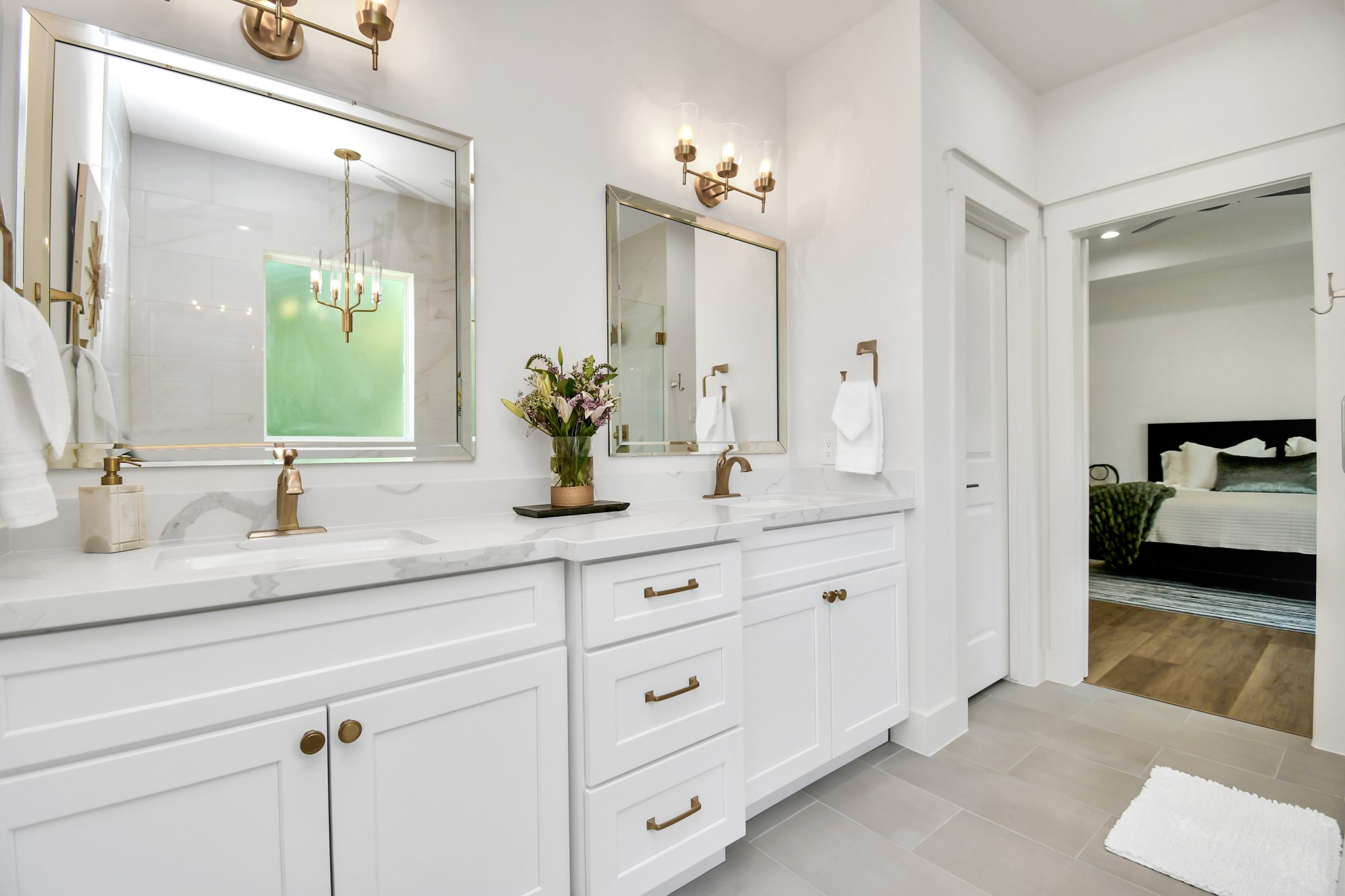 2512 Gray Street Houston, TX 77003 - Photo 31 of 46 This photo showcases a modern, elegant bathroom with double sinks, marble countertops, and brass fixtures. It features large mirrors, ample cabinet space, and a view into a connected bedroom with wood flooring.