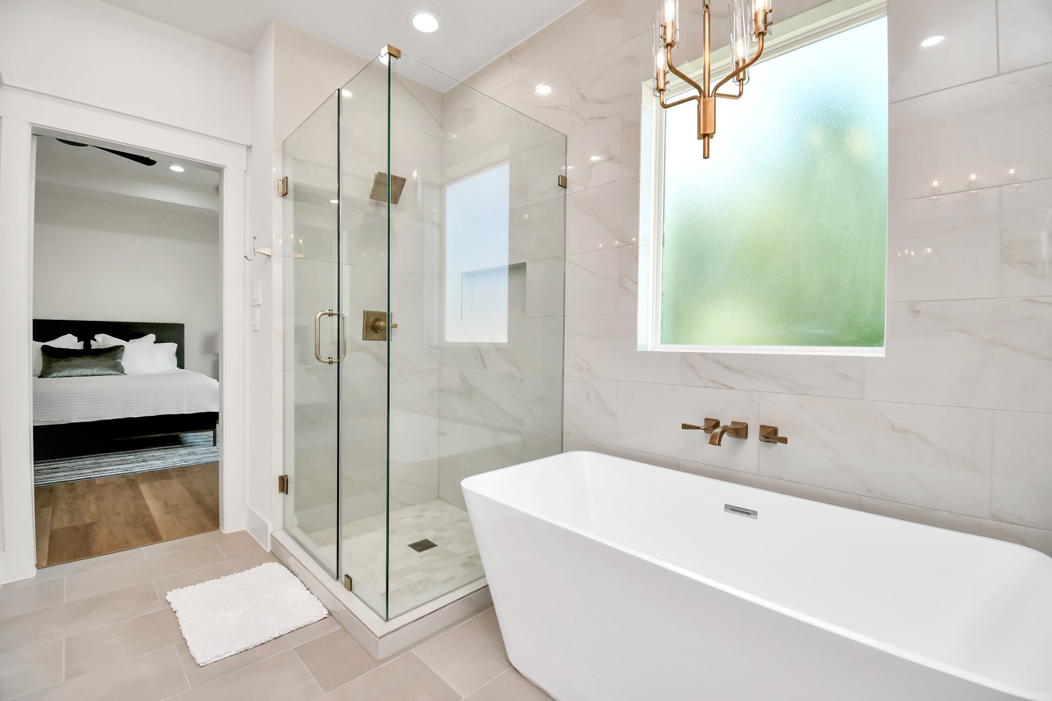 2512 Gray Street Houston, TX 77003 - Photo 32 of 46 This photo showcases a modern bathroom with a freestanding bathtub, a glass-enclosed shower, elegant fixtures, and a large frosted window for natural light. Adjacent is a bedroom with hardwood flooring.