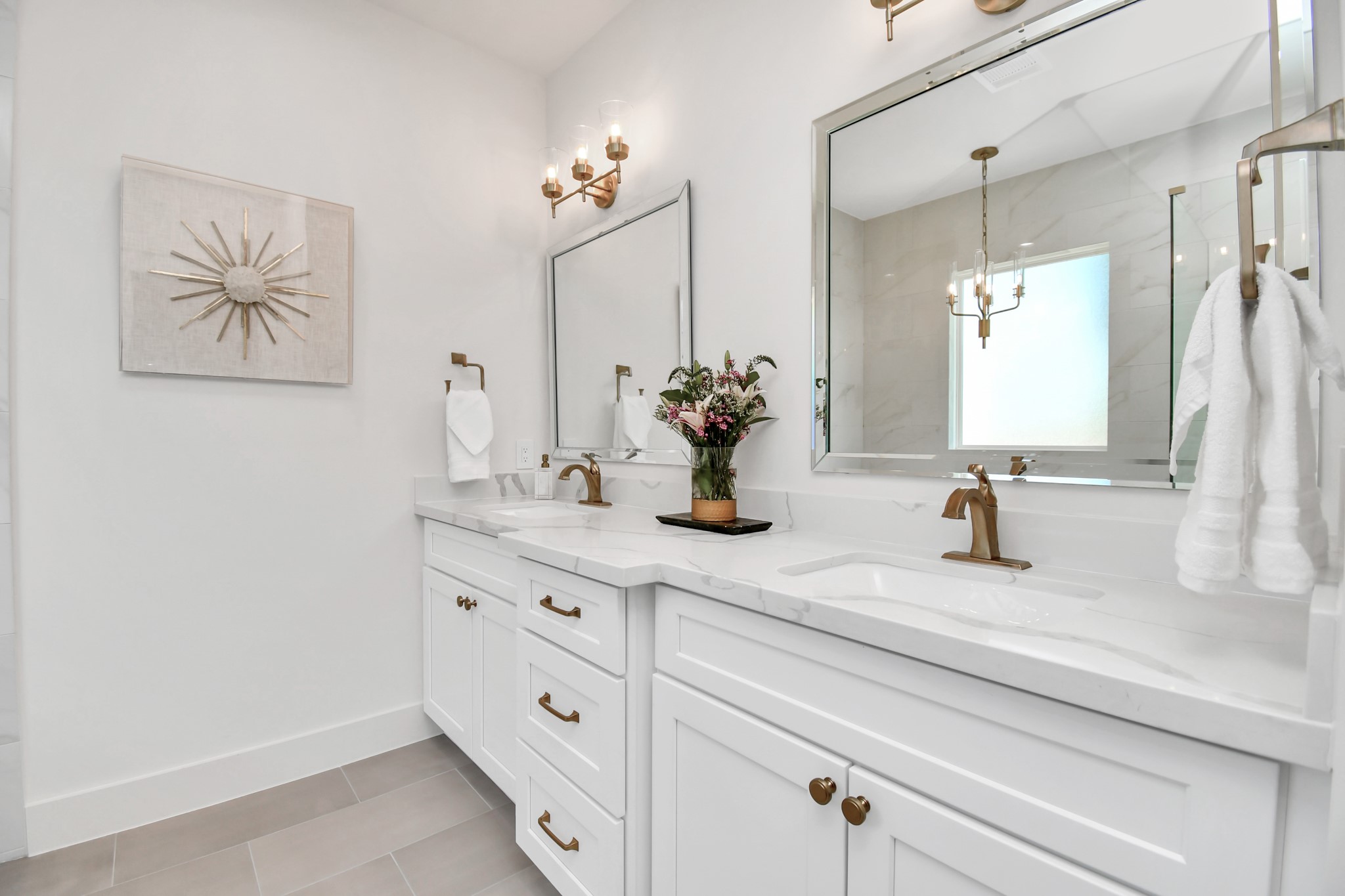 2512 Gray Street Houston, TX 77003 - Photo 33 of 46 This bathroom features a modern, elegant design with a double vanity, white cabinetry, and brass fixtures. The large mirrors and soft lighting enhance the spacious feel, complemented by decorative wall art and a vase of flowers.