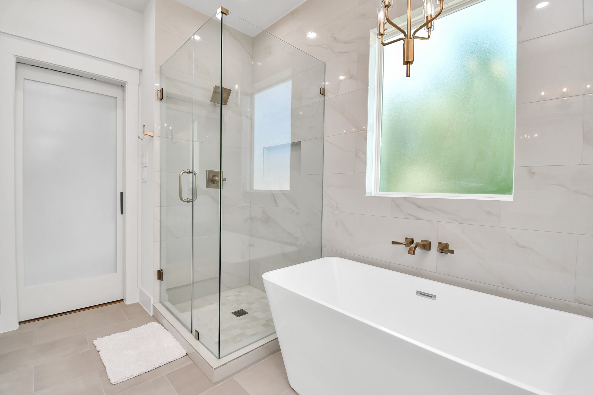 2512 Gray Street Houston, TX 77003 - Photo 34 of 46 This bathroom features a modern design with a spacious glass-enclosed shower and a sleek freestanding bathtub. It has elegant fixtures, a frosted window for privacy, and polished tile walls that add a luxurious touch.