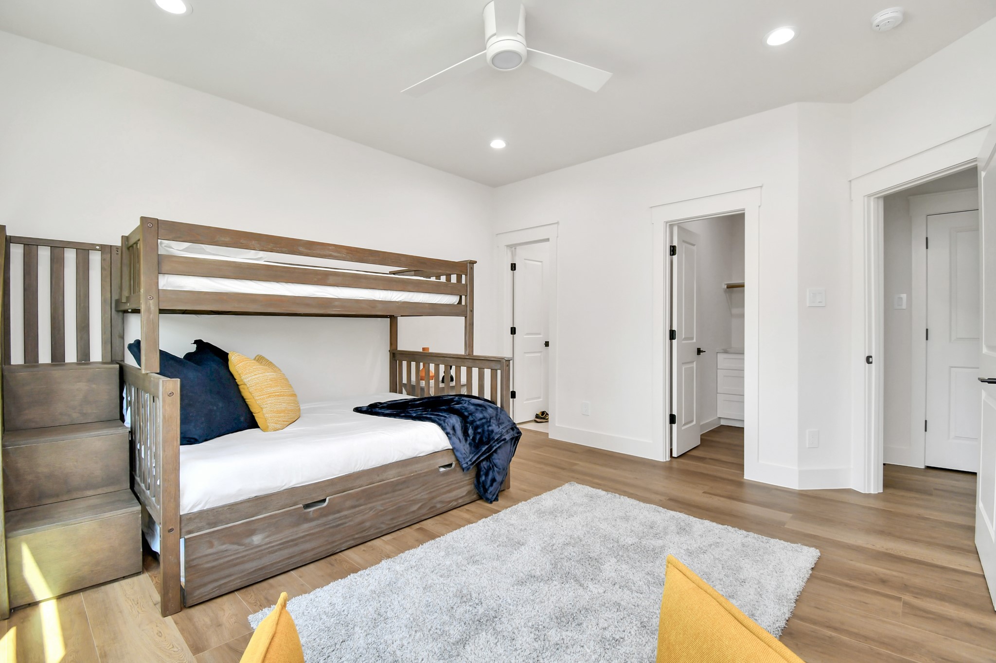 2512 Gray Street Houston, TX 77003 - Photo 36 of 46 This bright and spacious bedroom features a wooden bunk bed with storage stairs, modern ceiling fan, and a cozy rug. The room has light hardwood floors and neutral walls, with two doors leading to additional spaces, offering a versatile and welcoming environment.