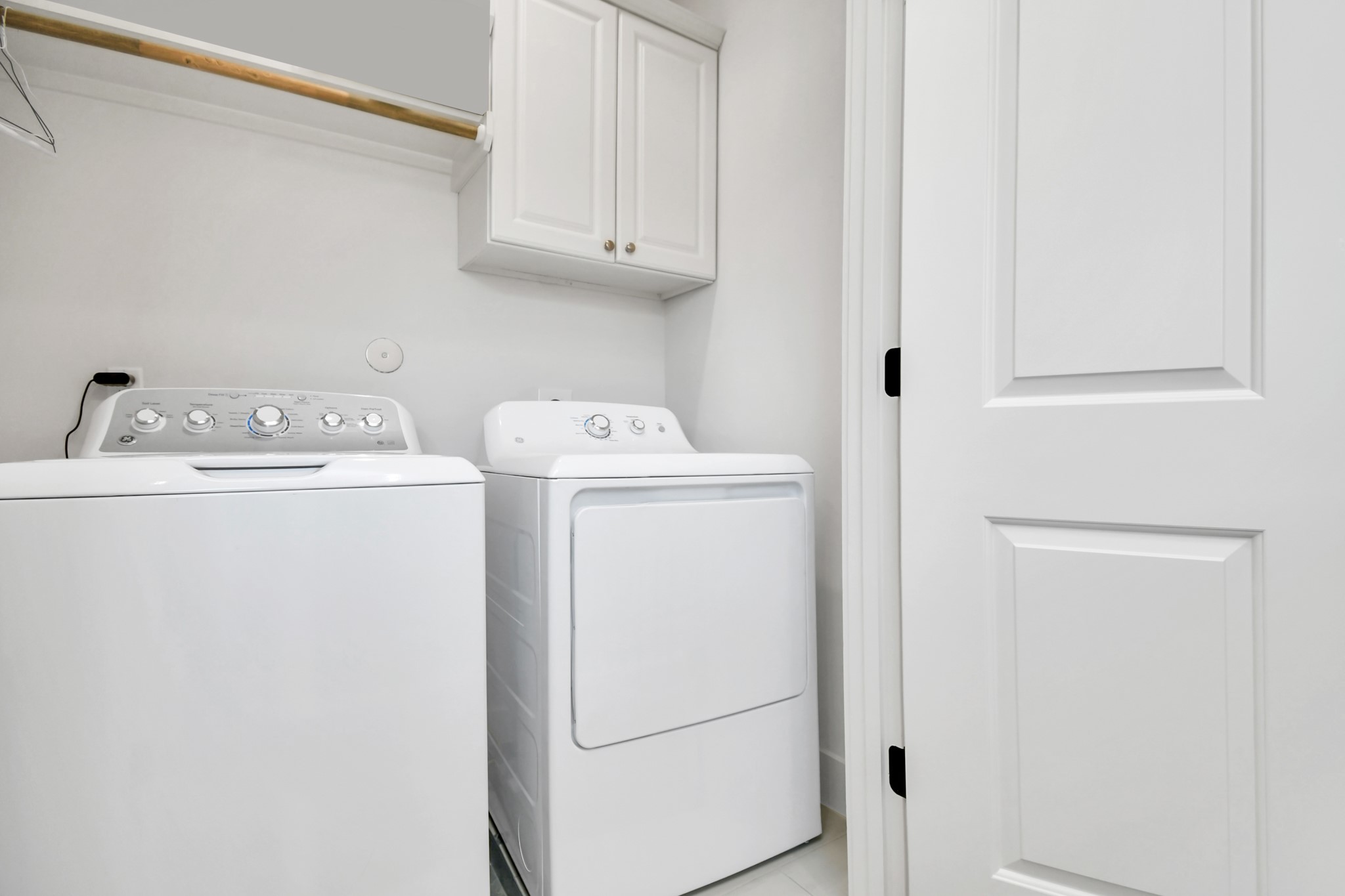 2512 Gray Street Houston, TX 77003 - Photo 38 of 46 This photo shows a compact laundry room featuring a modern washer and dryer set, white cabinetry for storage, and a hanging rod, all in a clean, bright space.