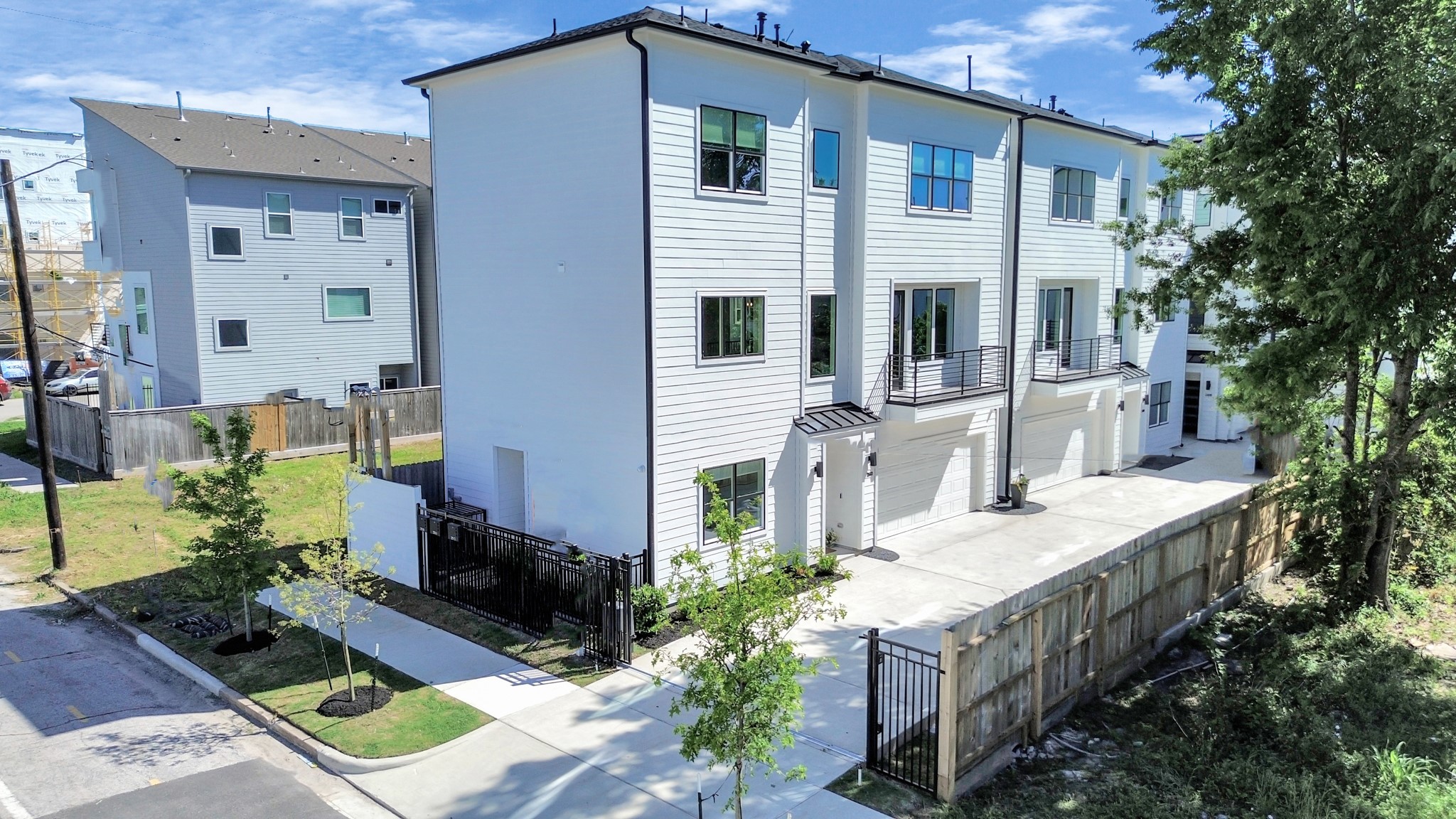 2512 Gray Street Houston, TX 77003 - Photo 42 of 46 This modern, multi-story townhouse features a sleek white exterior, large windows, and private balconies. It includes a gated driveway and small fenced yard, offering both security and outdoor space. The property is situated on a tree-lined street, providing a peaceful neighborhood setting.