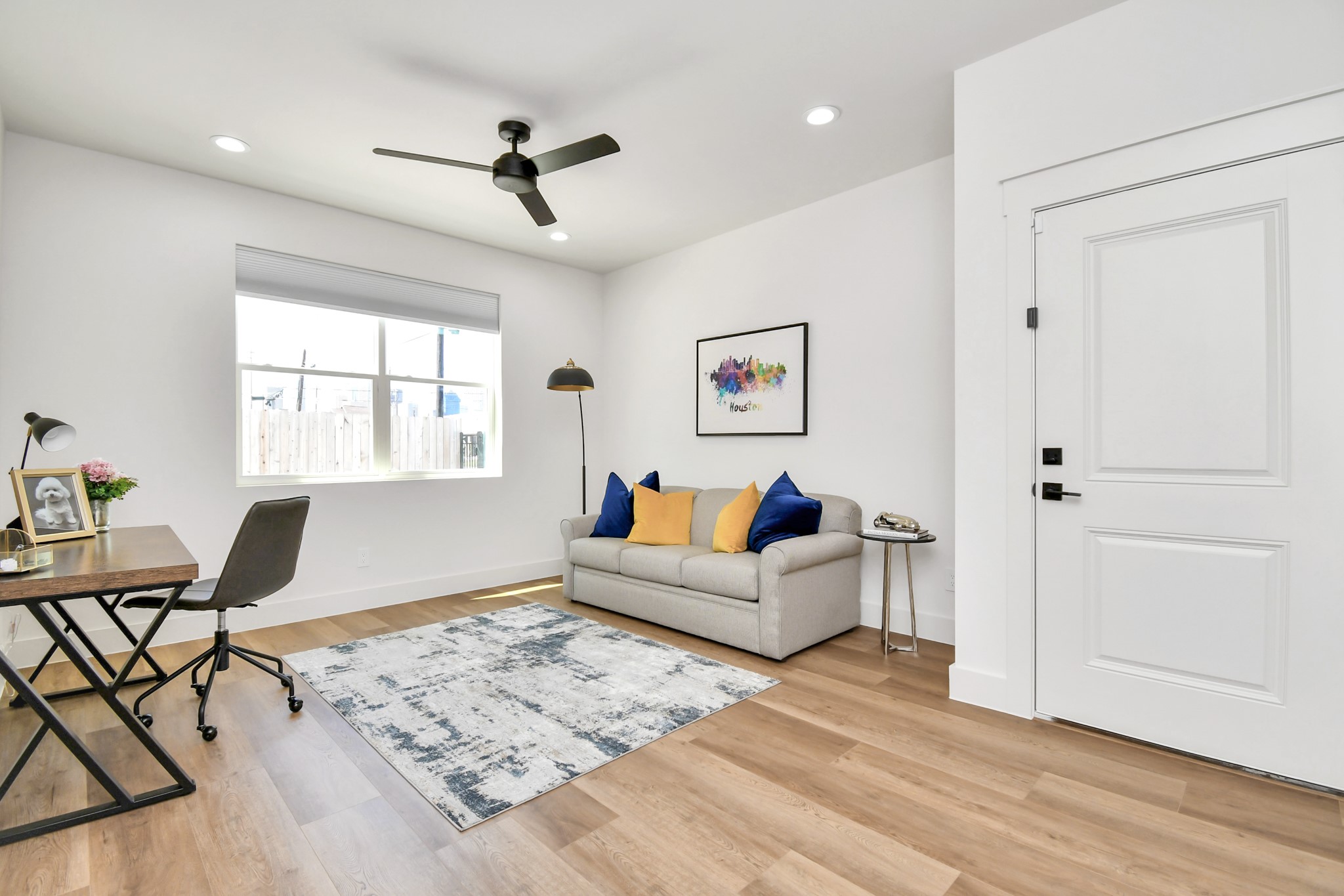 2512 Gray Street Houston, TX 77003 - Photo 5 of 46 This bright, airy room features hardwood floors, a cozy gray sofa with colorful cushions, and a modern desk setup. The large window lets in plenty of natural light, complemented by a ceiling fan and recessed lighting. Perfect for a home office or relaxation space.