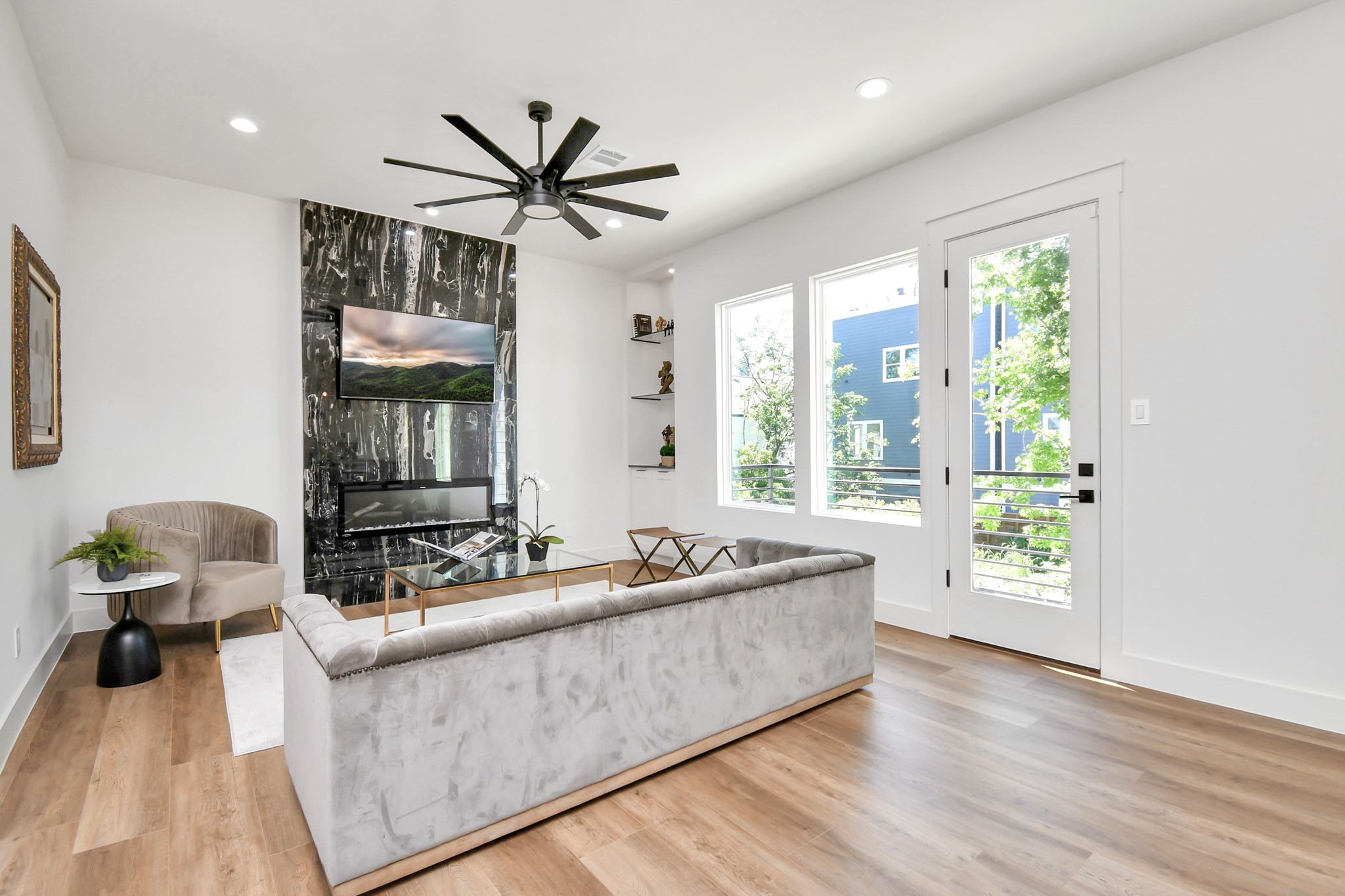 2512 Gray Street Houston, TX 77003 - Photo 9 of 46 This modern living room features a sleek design with a large marble accent wall, a wall-mounted TV, and a contemporary fireplace. Natural light floods through the large windows and glass door, highlighting the stylish furnishings and hardwood flooring.