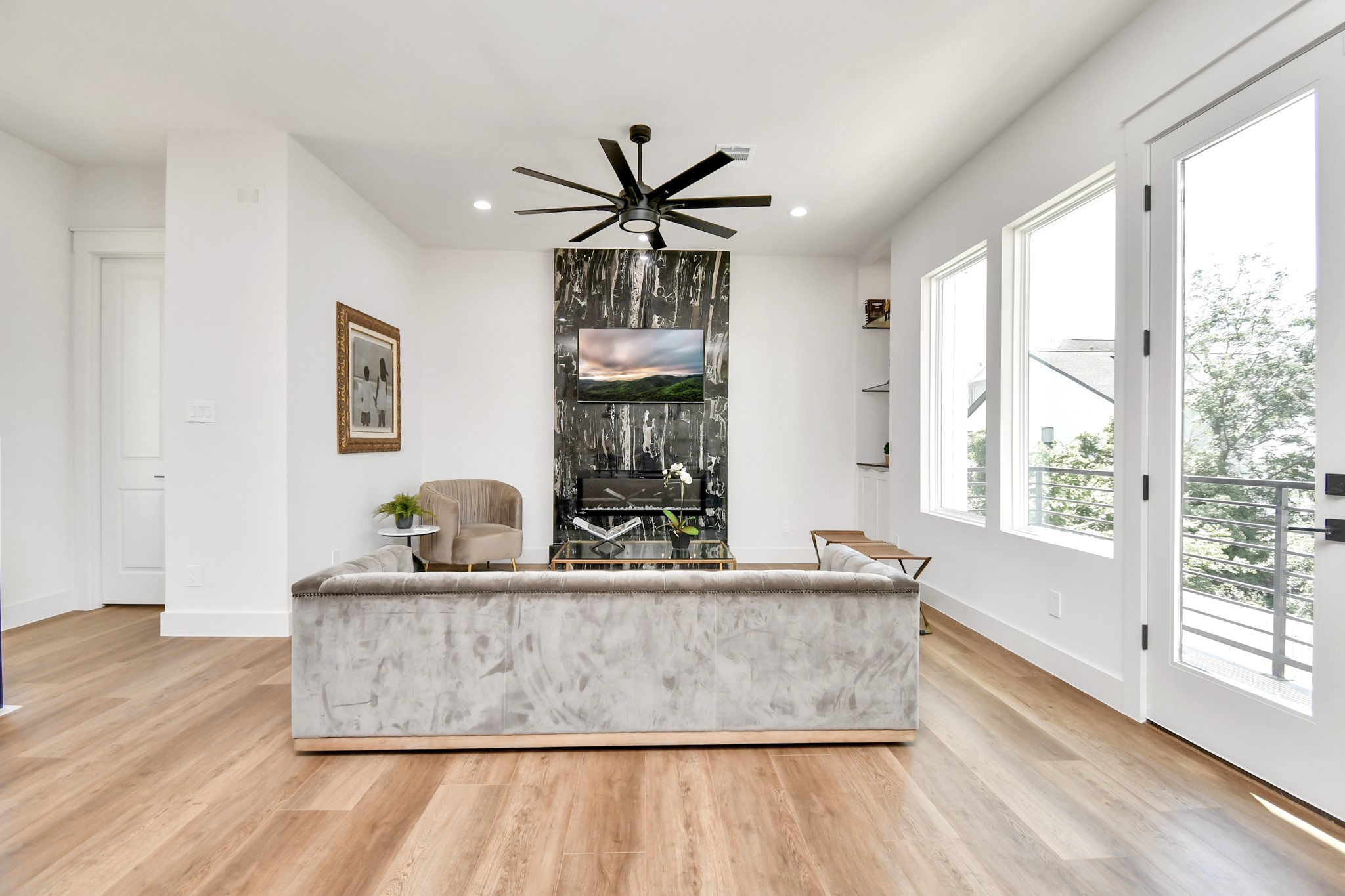 2512 Gray Street Houston, TX 77003 - Photo 10 of 46 This modern living room features sleek hardwood floors, a statement black marble fireplace with a mounted TV, and abundant natural light from large windows and glass doors that lead to a balcony. The space is tastefully furnished with a plush gray sofa and accent chair.