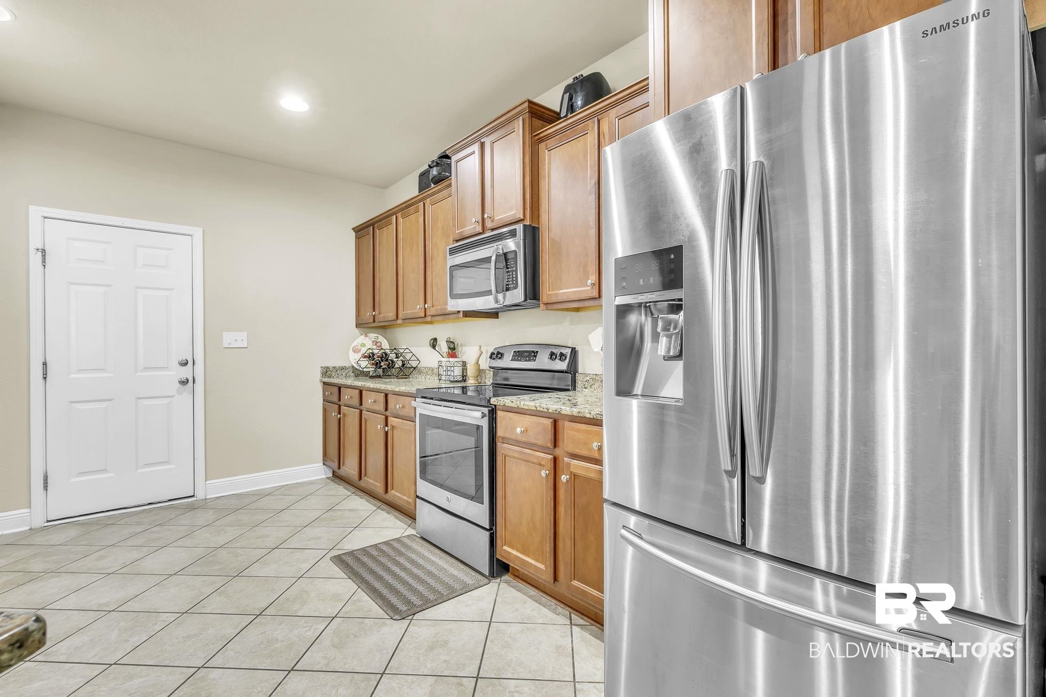 21439 Brick Stack Lane Fairhope, AL 36532 - Photo 14 of 32 Kitchen with light tile patterned floors, appliances with stainless steel finishes, light stone counters, and brown cabinets