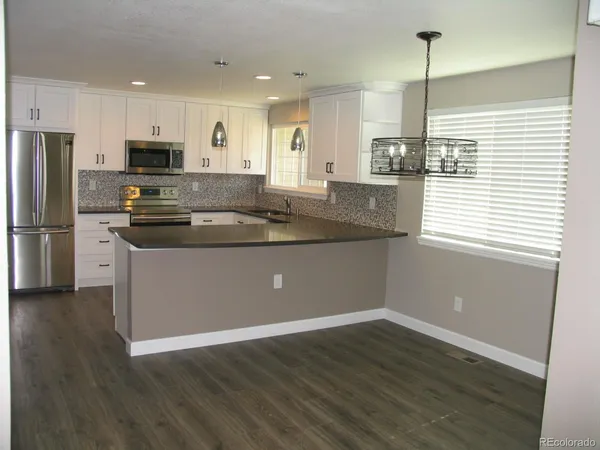 a kitchen with stainless steel appliances granite countertop a refrigerator a sink dishwasher a stove and white countertops with wooden floor