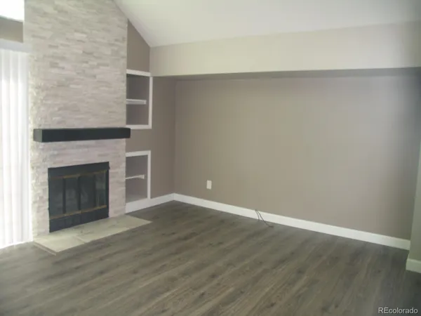 a view of an empty room with wooden floor and a fireplace