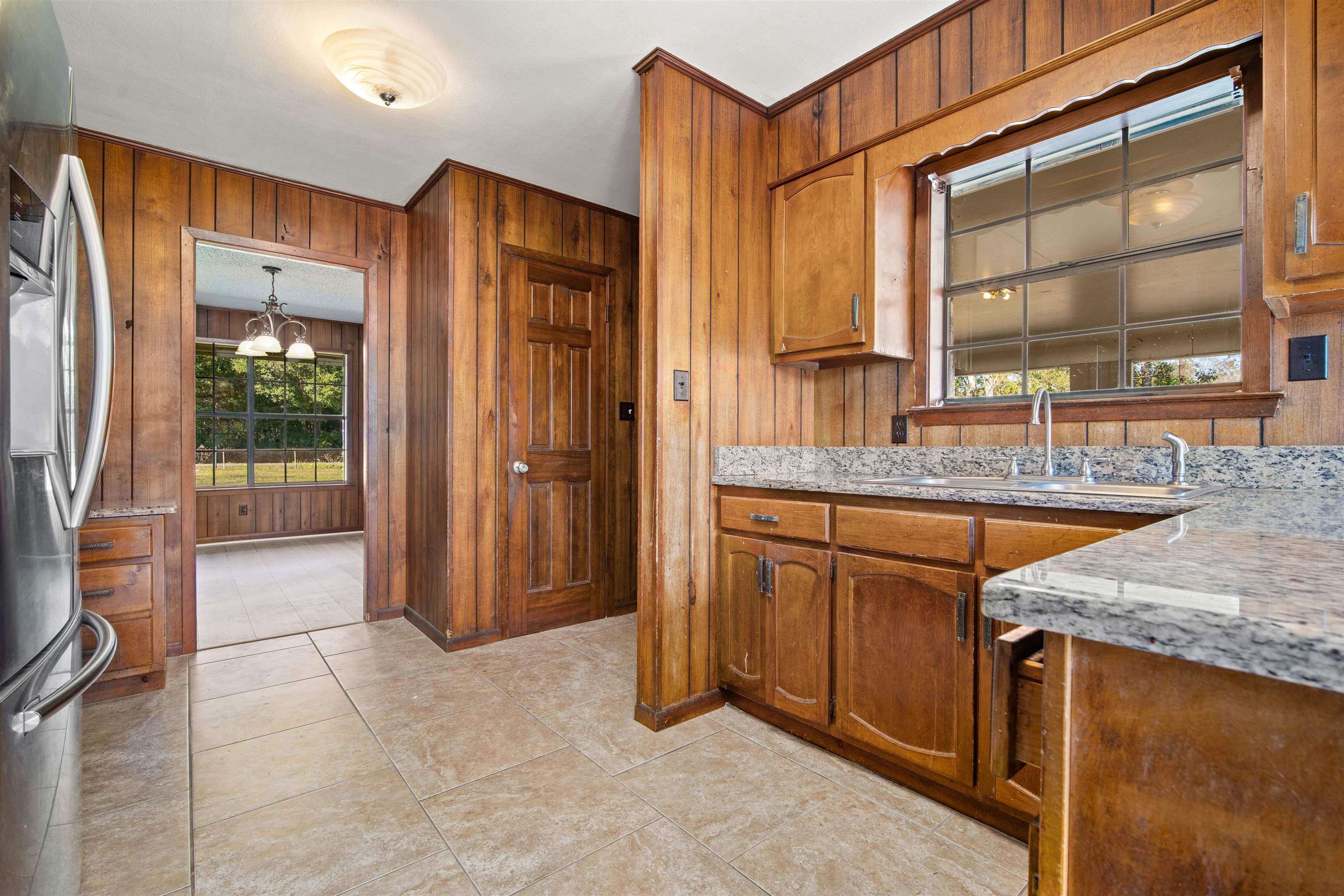 10285 Argyle Road Irvington, AL 36544 - Photo 11 of 28 Kitchen featuring wooden walls, brown cabinetry, stainless steel fridge with ice dispenser, light tile patterned flooring, and a chandelier