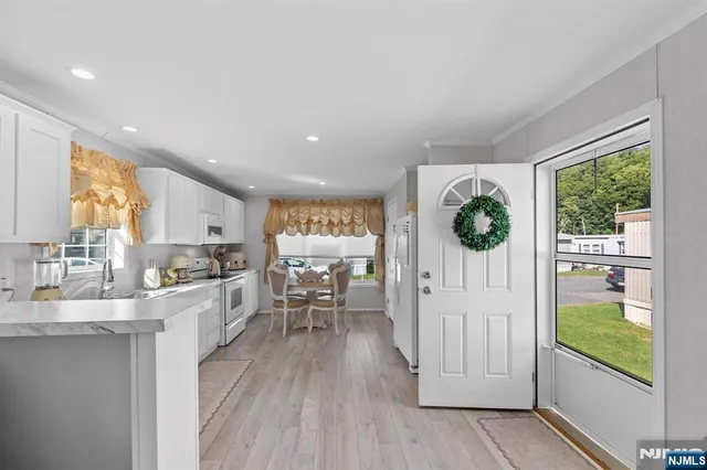 a kitchen with stainless steel appliances kitchen island granite countertop a refrigerator a sink a stove and white cabinets with wooden floor