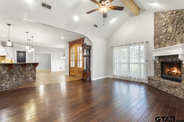 an empty room with wooden floor a fireplace a kitchen view and a chandelier