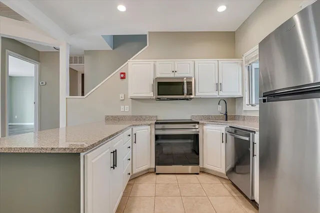 a kitchen with stainless steel appliances granite countertop a refrigerator a sink dishwasher a oven with white cabinets and wooden floor