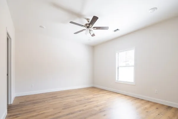 an empty room with wooden floor fan and windows