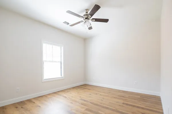 an empty room with wooden floor fan and windows