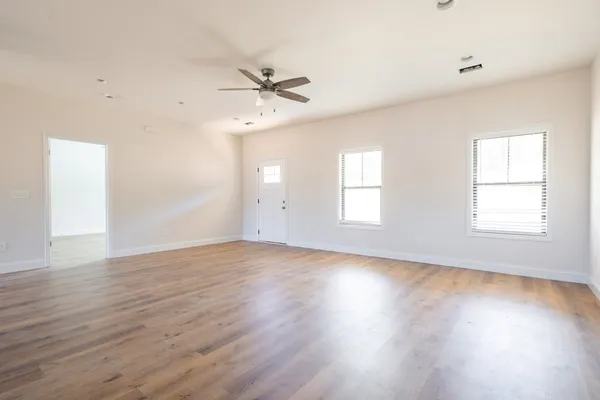 an empty room with wooden floor fan and windows