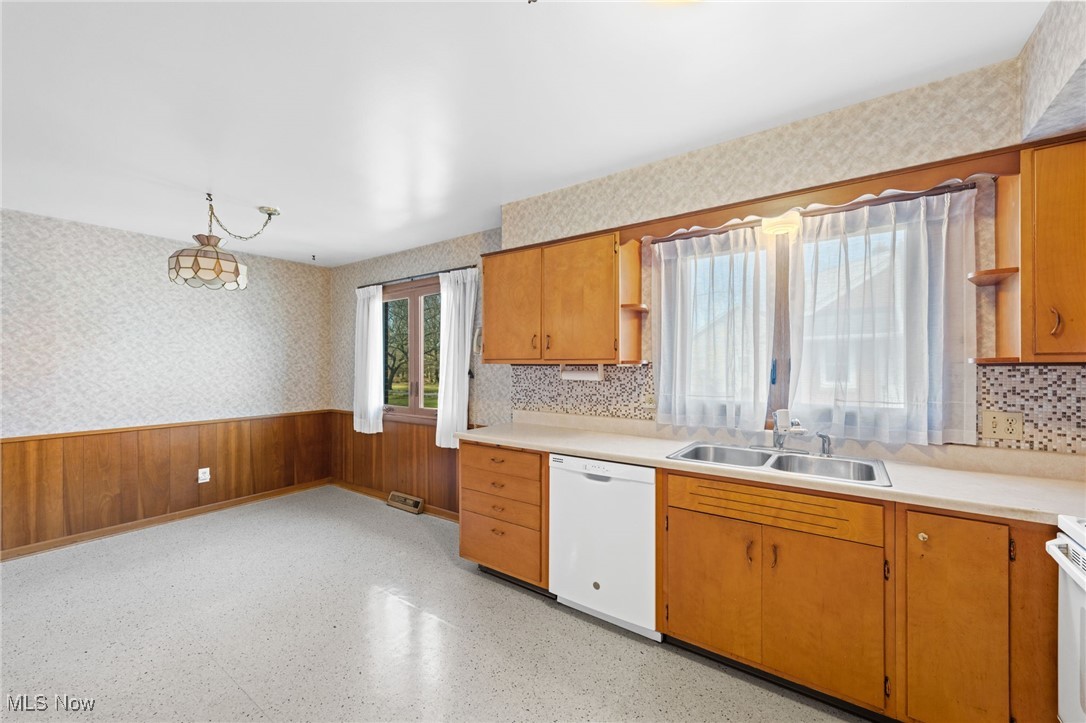 Kitchen featuring a wainscoted wall, light countertops, a sink, white appliances, and wallpapered walls