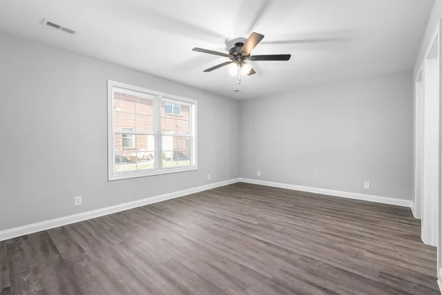 an empty room with wooden floor fan and windows