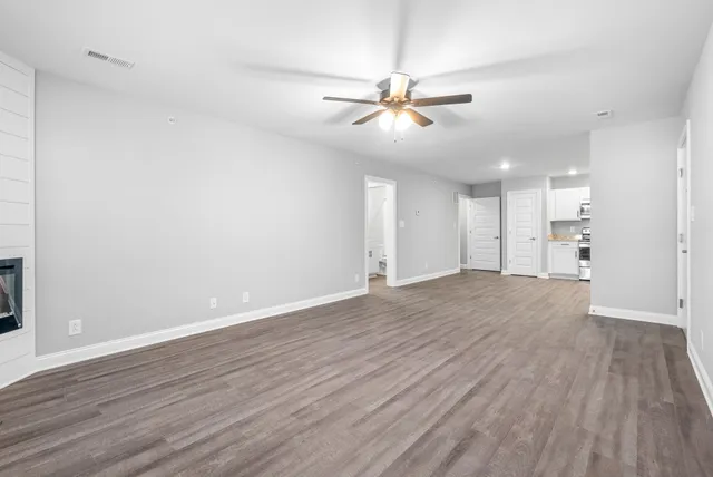a view of an empty room with wooden floor and a ceiling fan