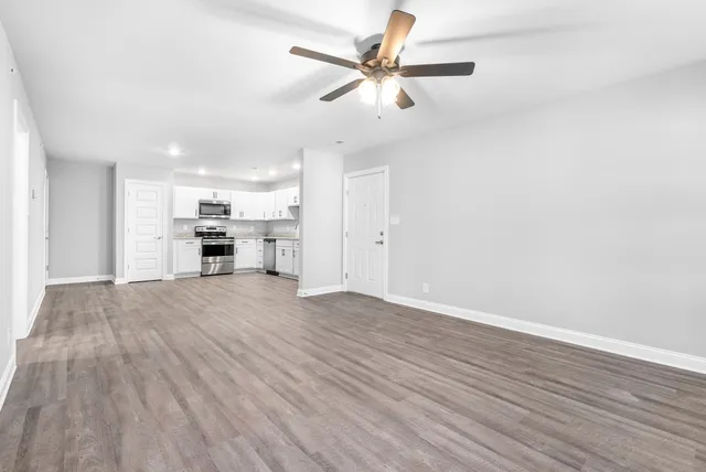 an empty room with wooden floor ceiling fan and windows