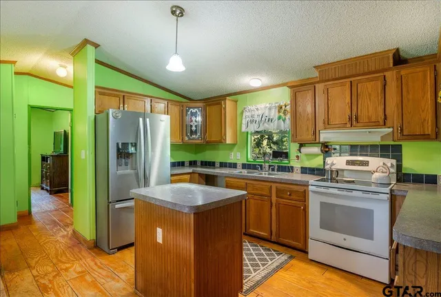 a kitchen with stainless steel appliances granite countertop a refrigerator a sink dishwasher a stove and white cabinets with wooden floor