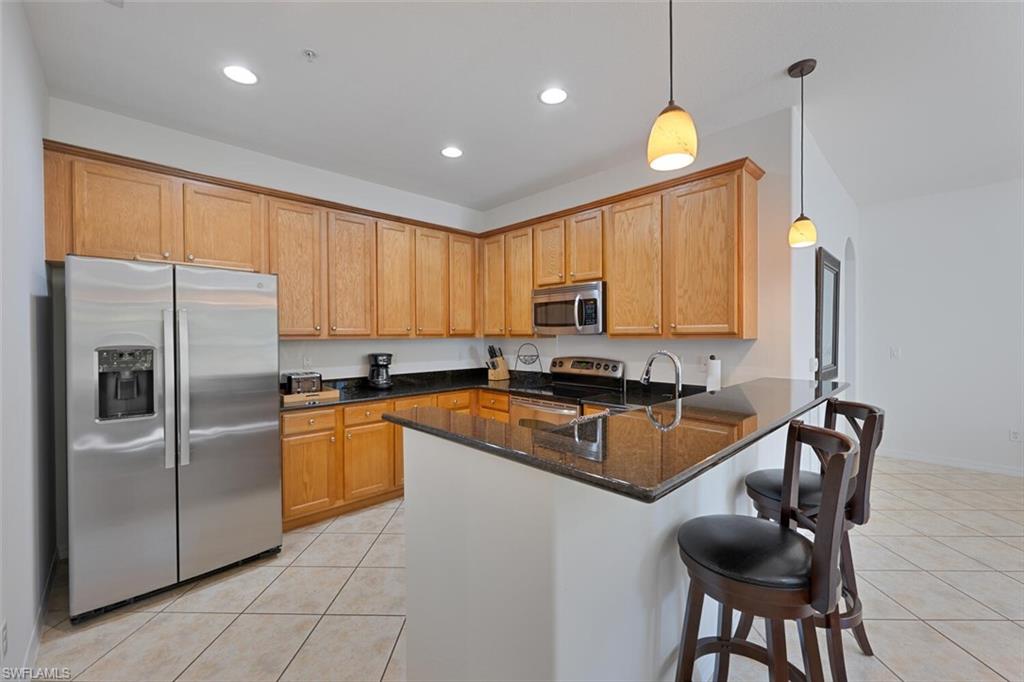8945 Malibu Street, Unit 204 Naples, FL 34113 - Photo 6 of 21 a kitchen with granite countertop a refrigerator a sink a stove a dining table and chairs with white cabinets